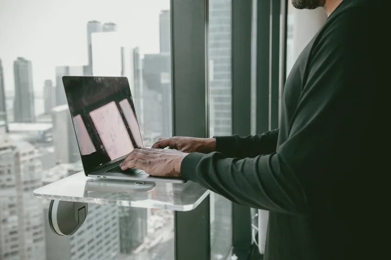 Person stands and types on a laptop by a window