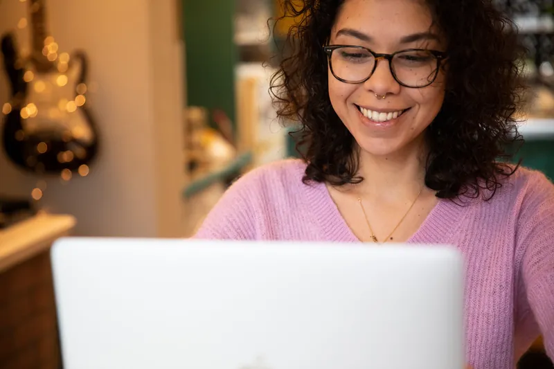 Person wears glasses and smiles at their laptop
